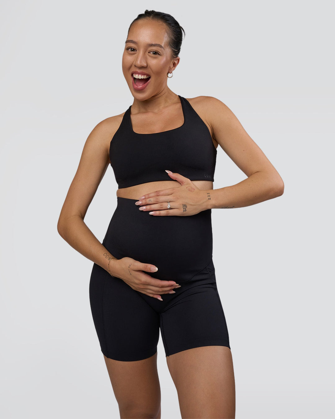 Woman wearing Elixir Ultra High-Rise Maternity 6&quot; Short Pockets - Black | Model:Kitahna | Size:S