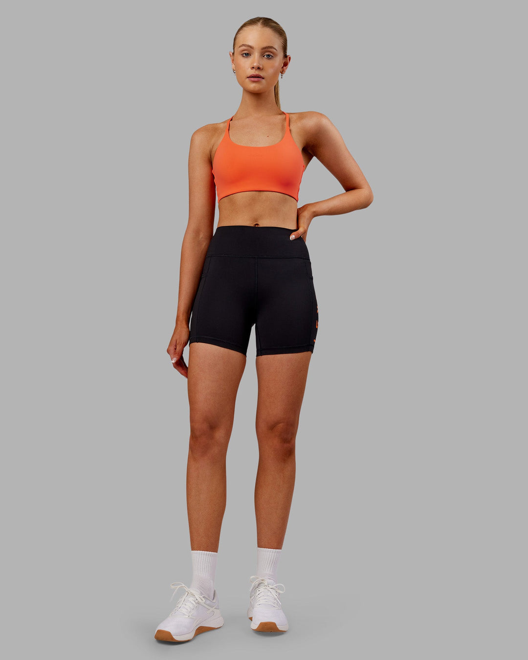 Woman wearing Rep Ultra High-Rise 4&quot; Short Pockets - Black-Ultra Orange | Model:Ella | Size:S