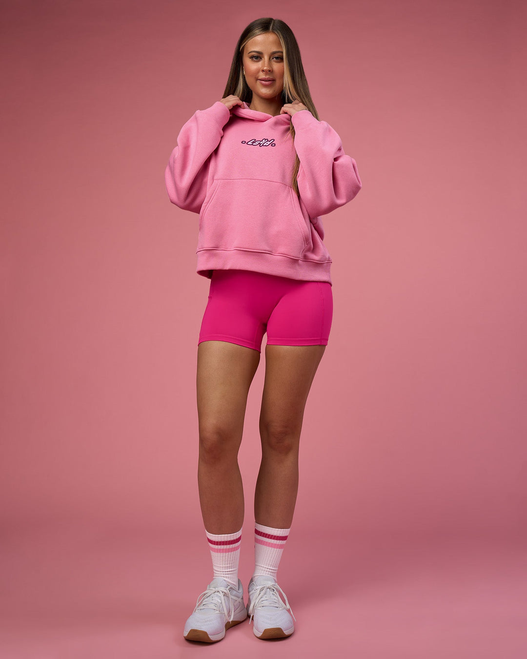 Woman wearing We Rise Post Train Cropped Hoodie - Candy Pink-Plum Caspia | Model:Tianah | Size:S