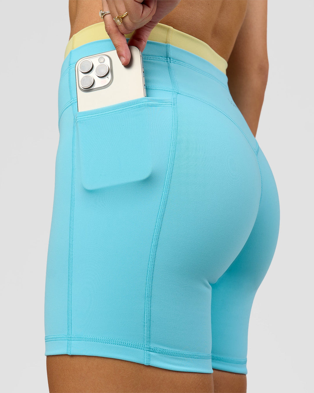 Woman wearing Lume Fusion Mid-Rise V Contour 6" Short Pockets - Baltic Sea-Lemon | Model:Grace | Size:XS