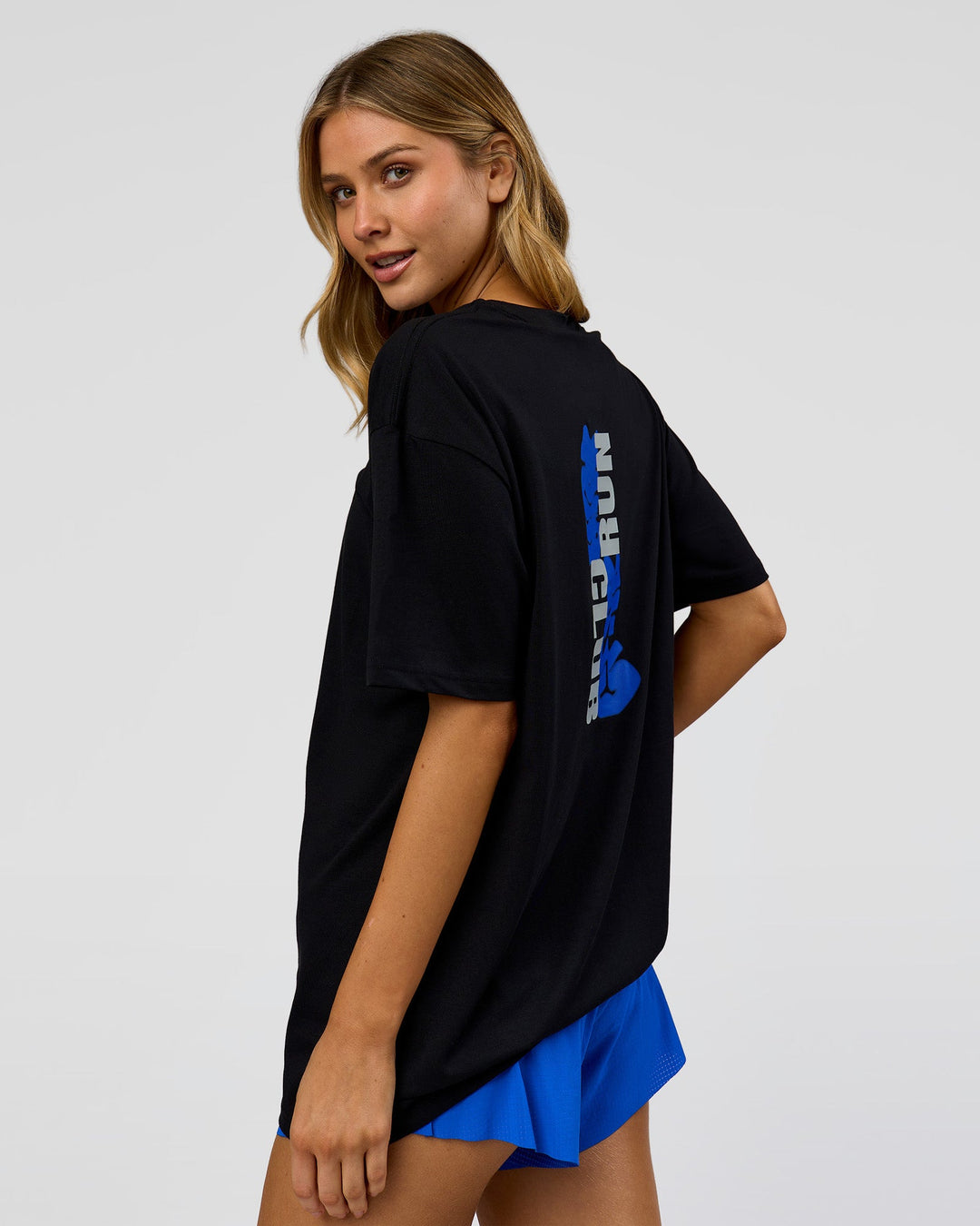 Woman wearing Run Club Elevate FLXCotton Oversized Tee - Black-Electric Indigo | Model:Leilani | Size:XS